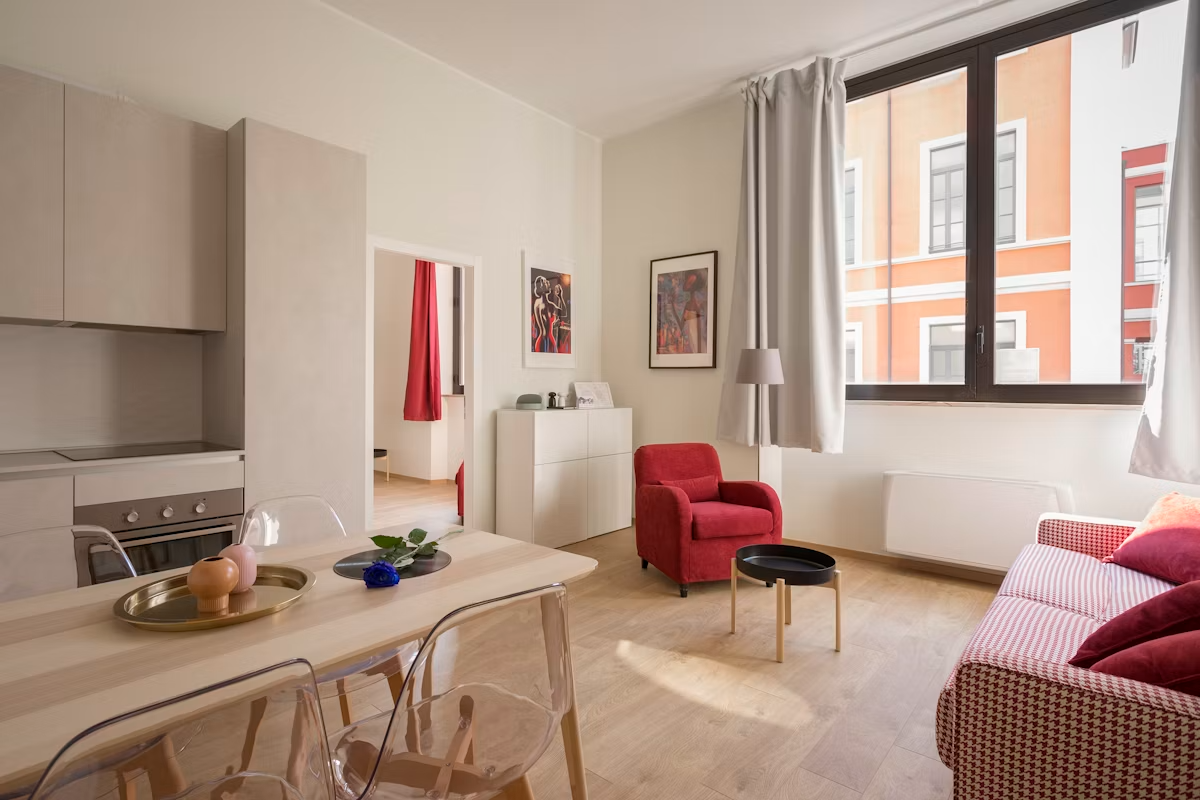 Modern studio apartment with kitchen, dining area, red armchair, and bed visible